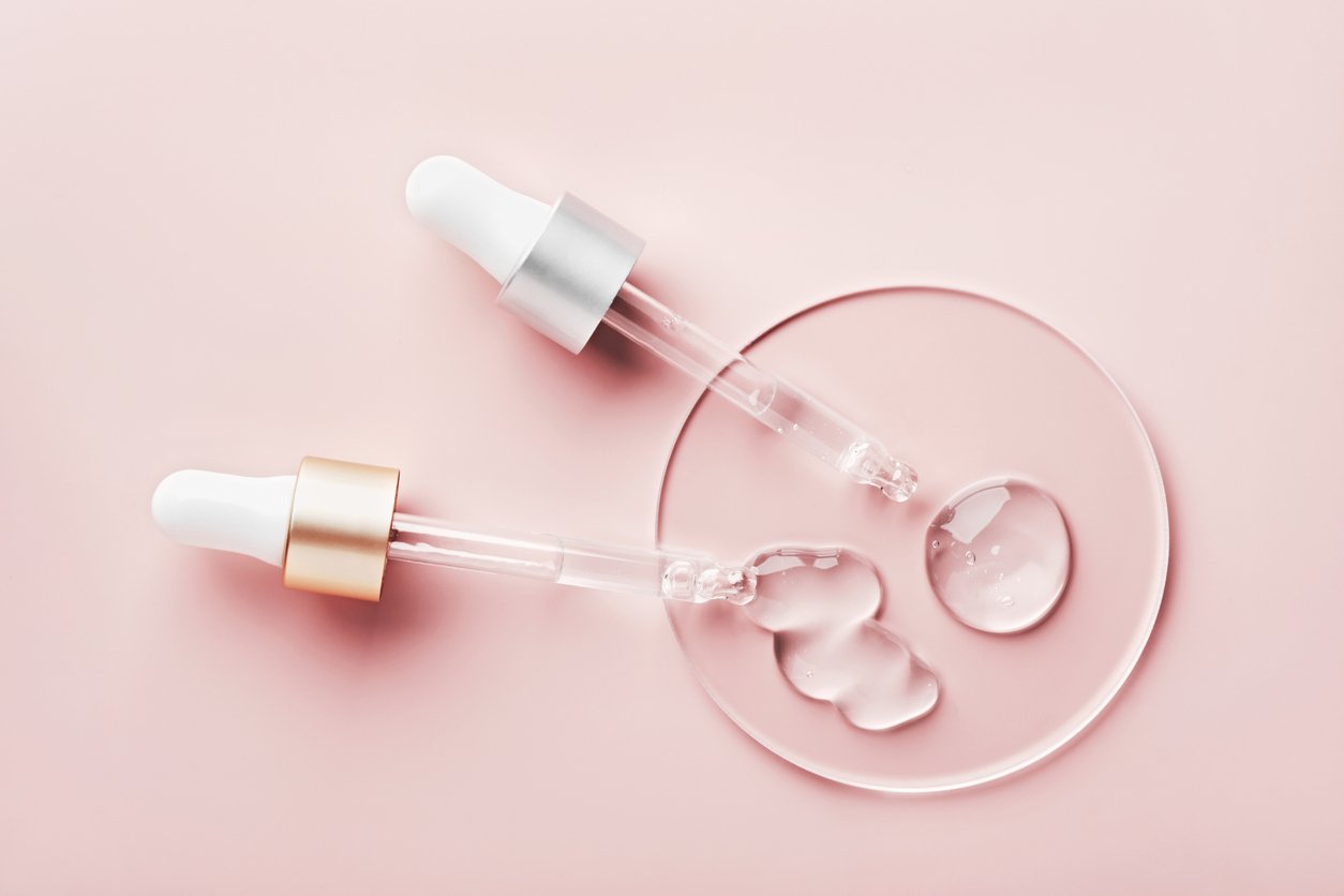Aus zwei Pipetten auf einer runden Glasscheibe tritt Flüssigkeit aus vor einem rosa Hintergrund